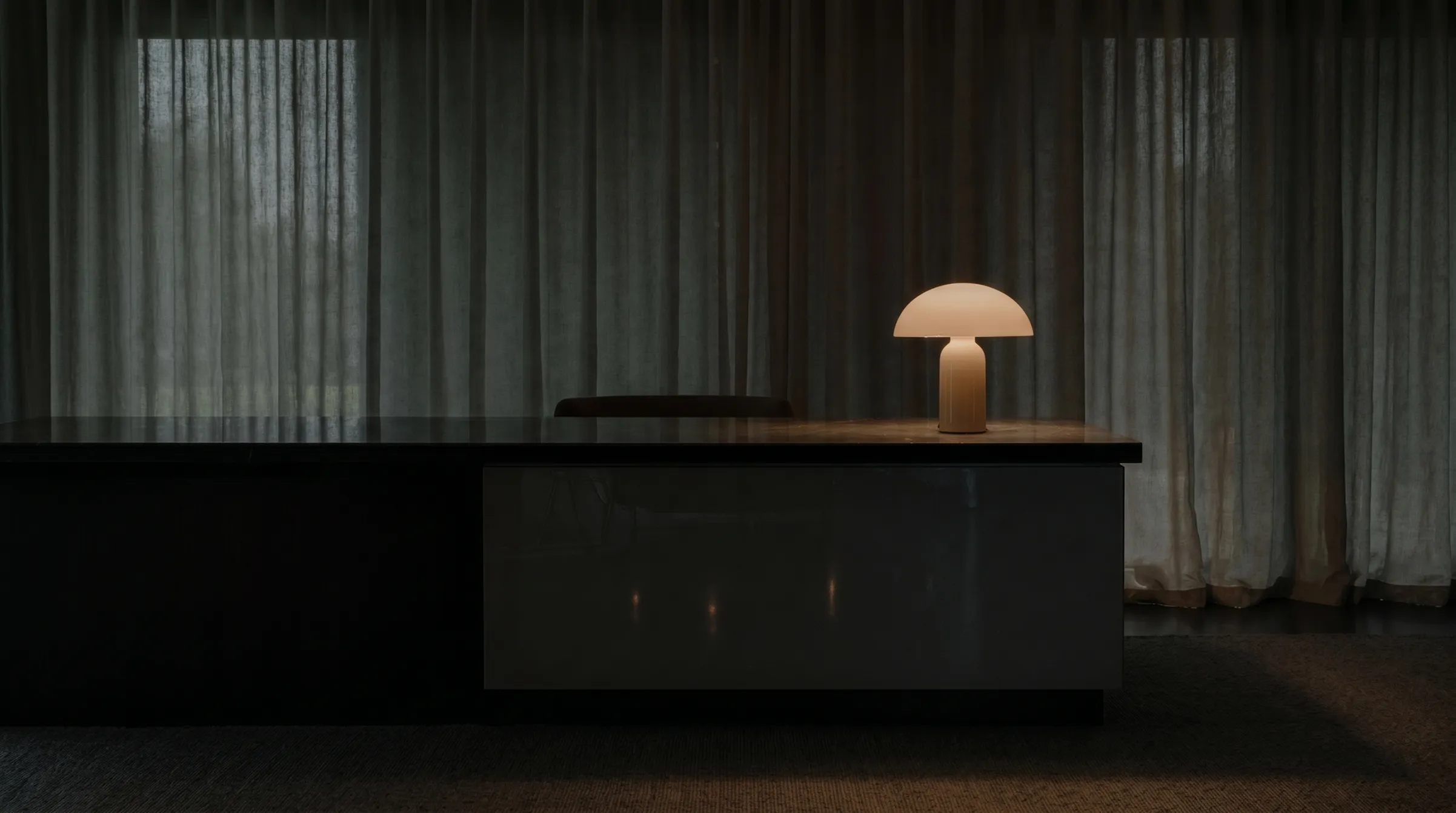 Modern desk with a glowing mushroom-shaped lamp in a dim room with sheer curtains.